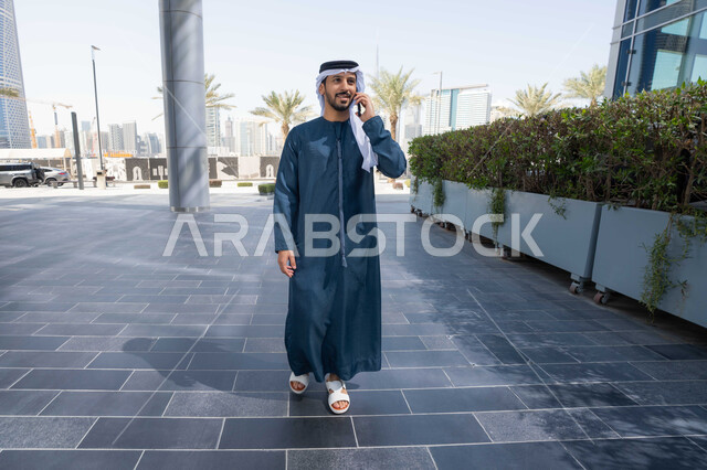 استخدام الهاتف المحمول والتقنيات الحديثه، نزهة وجولة فى الهواء الطلق ، برامج وتطبيقات الانترنت ، الدردشة مع الاصدقاء ، توثيق اللحظات السعيدة، رجل عربي خليجي اماراتي يرتدي الكندورة والغترة البيضاء، ينظر بتعابير السرور يقوم باستخدام الهاتف المحمول ، التسوق عبر تطبيقات الاونلاين  .