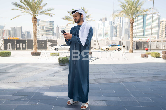 توثيق اللحظات السعيدة، استخدام الهاتف المحمول والتقنيات الحديثه، التسوق عبر تطبيقات الاونلاين ، اجراء مكالمة فيديو ، رجل عربي خليجي سعودية يرتدي الكندورة والغترة البيضاء، ينظر بتعابير السرور يقوم باستخدام الهاتف المحمول ، نزهة وجولة فى الهواء الطلق .