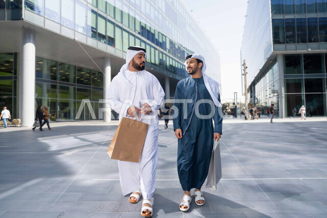 صداقات وتعارف ونقاشات وحوارات ، الشراء فى ايام التخفيضات ، ايماءات وتعابير السعادة ، قضاء أوقات ممتعة في الطبيعة ، التجول واستنشاق الهواء النقي في وقت النهار، صديقان عربيان خليجيان اماراتيان يرتديان الكندورة والغترة البيضاء ،  يحملان اكياس التسوق بتعابير السرور.