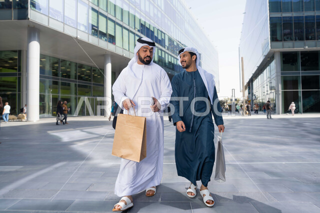 الشراء فى ايام التخفيضات ، ايماءات وتعابير السعادة ، قضاء أوقات ممتعة في الطبيعة ، التجول واستنشاق الهواء النقي في وقت النهار، صداقات وتعارف ونقاشات وحوارات ، صديقان عربيان خليجيان اماراتيان يرتديان الكندورة والغترة البيضاء ،  يحملان اكياس التسوق بتعابير السرور.