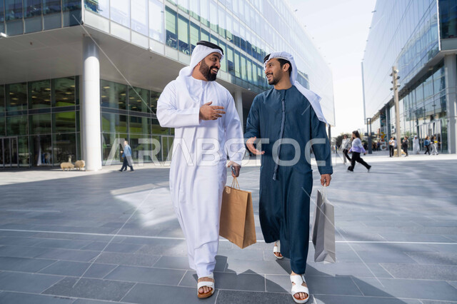 الاستمتاع بالشراء والتسوق ، قضاء أوقات ممتعة في الطبيعة ، التجول واستنشاق الهواء النقي في وقت النهار، صداقات وتعارف ونقاشات وحوارات ، مفهوم الأناقة والاهتمام بالمظهر الخارجي ،  صديقان عربيان خليجيان اماراتيان يرتديان الكندورة والغترة البيضاء ،  يحملان اكياس التسوق بتعابير السرور.