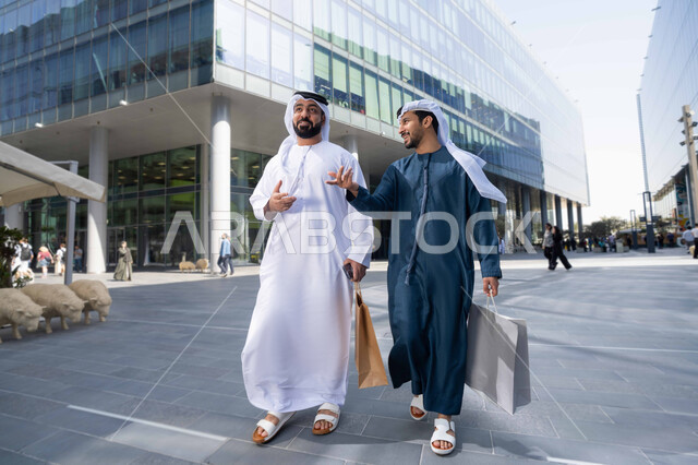 قضاء أوقات ممتعة في الطبيعة ، الاستمتاع والتجول واستنشاق الهواء النقي في وقت النهار، صداقات وتعارف ونقاشات وحوارات ، مفهوم الأناقة والاهتمام بالمظهر الخارجي ،  صديقان عربيان خليجيان اماراتيان يرتديان الكندورة والغترة البيضاء ،  يحملان اكياس التسوق بتعابير السرور.