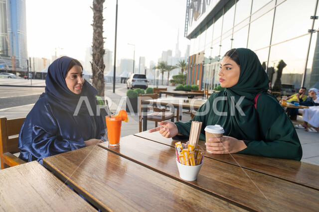 الحصول على الهدية والتهنئة ، أعياد ومناسبات ومفاجآت سعيدة ،  يوم الام السعيد ، ايماءات الرضى والسرور، تقديم الهدايا والأزهار للأمهات ، مفهوم حب الأم والإحسان إليها، صورة مقربة لامراة عربية خليجية اماراتية ترتدي العباءة تجلس فى احدي المقاهي ، تقوم باحضار هدية لوالدتها .