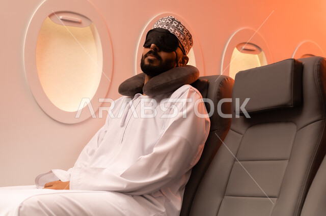 النوم والراحه والاسترخاء داخل الطائره, بورتريه مقرب من الجانب لرجل عربي خليجي عماني يرتدي الدشداشه والكمه يجلس على كرسيه ويضع الماسك الاسود على عينه ومخده السفرحول رقبته, الطيران الخليجي العماني