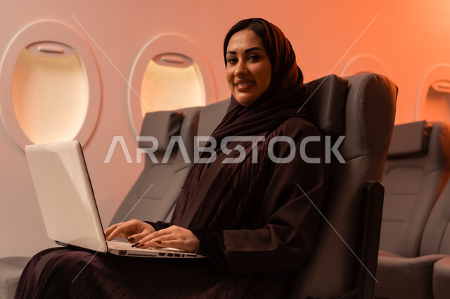 التواصل عن بعد مع الاهل و الأصدقاء، مفهوم اداره الاعمال والترفيه والتسليه عن بعد، السياحة في إجازة الصيف, بورتريه مقرب من الجانب لشابه عربيه خليجيه عمانيه تعمل على جهاز الايباد المحمول وهي تجلس على كرسيها داخل الطائره, الخطوط الجويه العمانيه