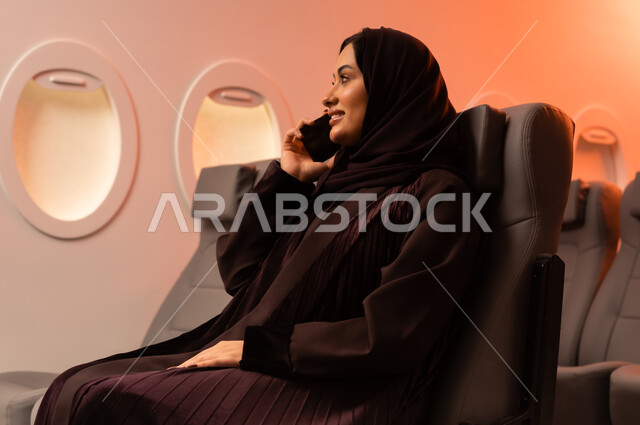 التواصل عن بعد مع الاهل و الأصدقاء، الإجابة والرد على الاتصالات باستخدام الهاتف المحمول، السياحة في إجازة الصيف, بورتريه مقرب من الجانب لشابه عربيه خليجيه عمانيه تمسك بهاتفهها المحمول على كرسيها داخل الطائره, الخطوط الجويه العمانيه