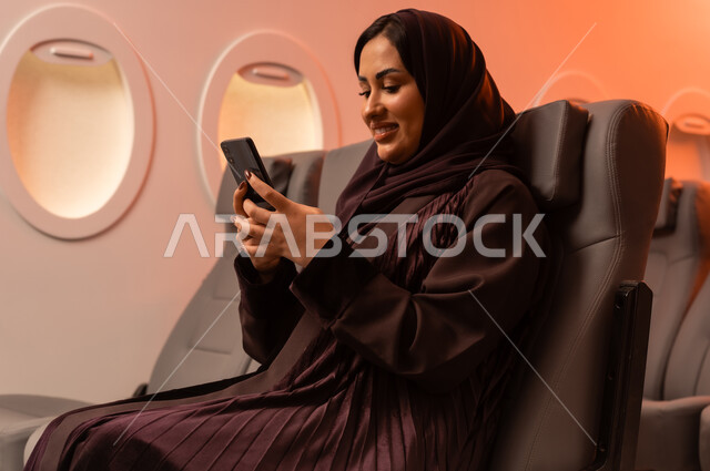 التواصل عن بعد مع الاهل و الأصدقاء، الإجابة والرد على الاتصالات باستخدام الهاتف المحمول، السياحة في إجازة الصيف, بورتريه مقرب من الجانب لشابه عربيه خليجيه عمانيه تمسك بهاتفهها المحمول على كرسيها داخل الطائره, الخطوط الجويه العمانيه