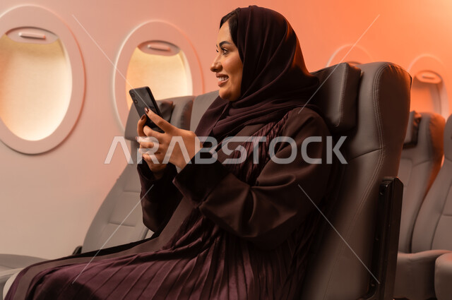 التواصل عن بعد مع الاهل و الأصدقاء، الإجابة والرد على الاتصالات باستخدام الهاتف المحمول، السياحة في إجازة الصيف, بورتريه مقرب من الجانب لشابه عربيه خليجيه عمانيه تمسك بهاتفهها المحمول على كرسيها داخل الطائره, الخطوط الجويه العمانيه