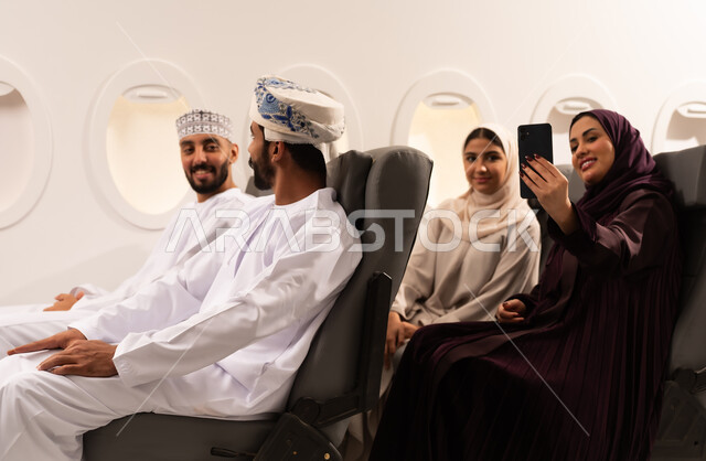 قضاء أوقات ممتعة داخل الطائرة ، بورتريه مقرب من الجانب لمسافرون من العرب العمانيون الخليجيون داخل مقصورة الطائرة يرتدون الزي العماني، ايماءات تدل على الفرح والسعادة ، رحلات سياحية جويه ممتعة، عطلة صيفية عائلية، الخطوط الجوية العمانيه، سياحة وسفر