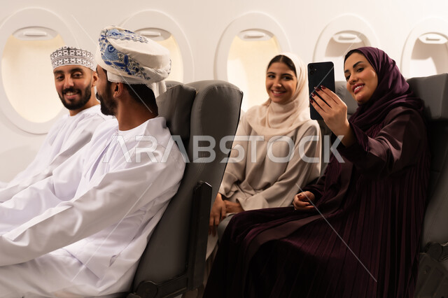 قضاء أوقات ممتعة داخل الطائرة ، بورتريه مقرب من الجانب لمسافرون من العرب العمانيون الخليجيون داخل مقصورة الطائرة يرتدون الزي العماني، ايماءات تدل على الفرح والسعادة ، رحلات سياحية جويه ممتعة، عطلة صيفية عائلية، الخطوط الجوية العمانيه، سياحة وسفر
