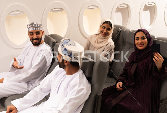 قضاء أوقات ممتعة داخل الطائرة ، بورتريه مقرب من الجانب لمسافرون من العرب العمانيون الخليجيون داخل مقصورة الطائرة يرتدون الزي العماني، ايماءات تدل على الفرح والسعادة ، رحلات سياحية جويه ممتعة، عطلة صيفية عائلية، الخطوط الجوية العمانيه، سياحة وسفر