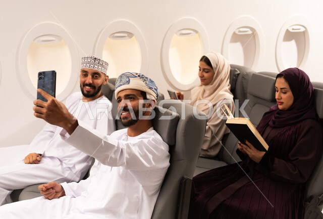 قضاء أوقات ممتعة داخل الطائرة ، بورتريه مقرب من الجانب لمسافرون من العرب العمانيون الخليجيون داخل مقصورة الطائرة يرتدون الزي العماني، ايماءات تدل على الفرح والسعادة ، رحلات سياحية جويه ممتعة، عطلة صيفية عائلية، الخطوط الجوية العمانيه، سياحة وسفر