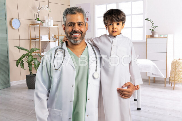صورة لطبيب خليجي سعودي مع طفل صغير ، ينظران إلى الكاميرا ، مفهوم الطب والرعاية الصحية ، الفحص الطبي للأطفال ، تقديم الرعاية والخدمات الصحية ، مهن ووظائف طبية ، موعد مع الطبيب لتلقي العلاج