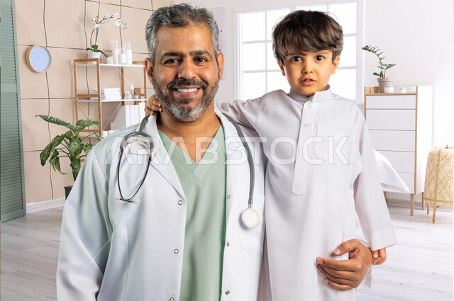 صورة لطبيب خليجي سعودي مع طفل صغير ، ينظران إلى الكاميرا ، مفهوم الطب والرعاية الصحية ، الفحص الطبي للأطفال ، تقديم الرعاية والخدمات الصحية ، مهن ووظائف طبية ، موعد مع الطبيب لتلقي العلاج