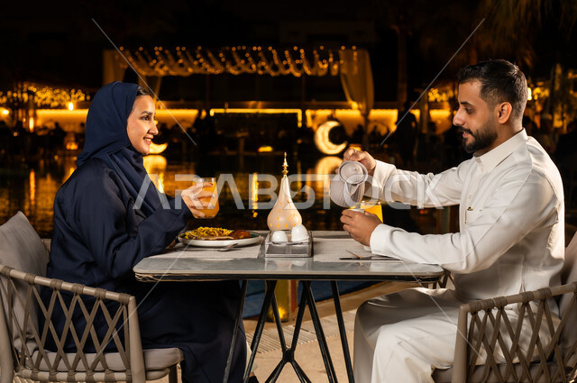 أجواء عائلية سعيدة، الاستمتاع بتناول المشروبات خارج المنزل,عائله عربيه خليجيه سعودية ترتدي الزي التقليدي تجلس في مطعم فاخر , زينه و ديكور تقليدي لاستقبال شهر رمضان المبارك, رجل خليجي يقوم بصب المشروب, ايماءات السعاده و السرور