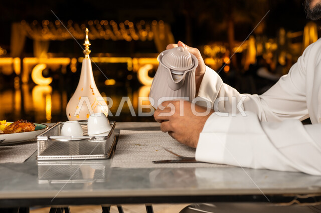 أجواء عائلية دينية، الاستمتاع بتناول المشروبات خارج المنزل, صورة مقربة ليد رجل عربية خليجي سعودي يقوم بصب المشروب الساخن , زينه و ديكور تقليدي لاستقبال شهر رمضان المبارك