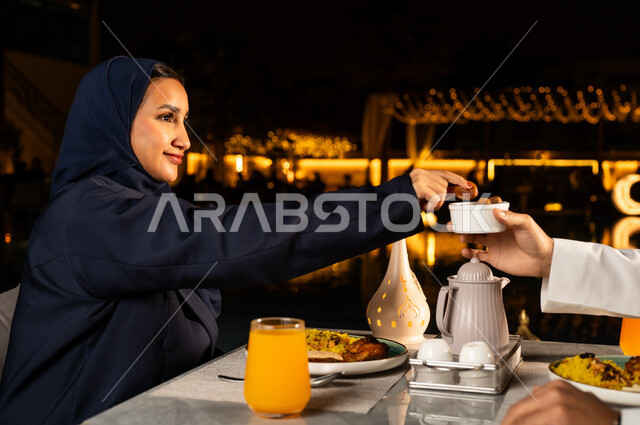 سفرة مليئة باصناف من المأكولات الشهية, إيماءات السعادة و السرور، أجواء دينية رمضانية، صورة مقربة لامراة عربيه خليجيه سعودية مبتسمه ترتدي العباءه تقوم بتناول التمر عند اذان المغرب ، أداء فريضة الصيام