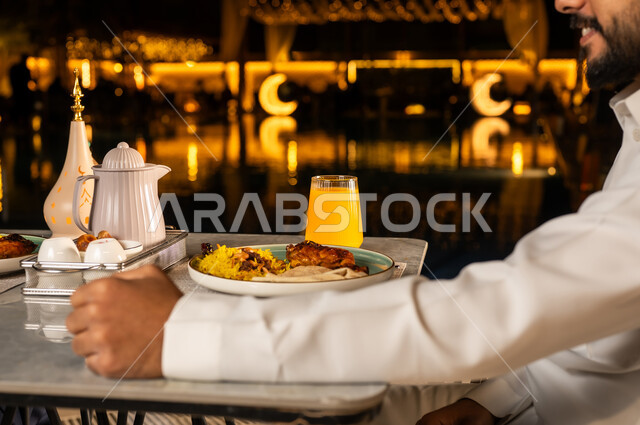 Preparing and setting up the iftar table, the dining table filled with delicious food and appetizers, Ramadan decorations and atmosphere, a close-up of the hand of a Saudi Arabian Gulf man sitting in front of the dining table waiting for the iftar cannon, enjoying drinks, celebrating the arrival of the month of goodness