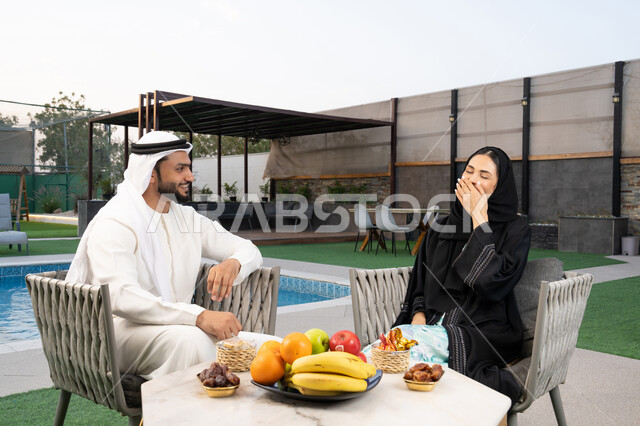 الجلوس في إحدى الشاليهات الاماراتية الراقية, رجل عربي خليجي اماراتي يرتدي الكندورة والغترة يقوم بتبادل الأحاديث مع زوجته في الهواء الطلق, قضاء أوقات عائلية ممتعة, التفاهم والترابط الفكري بين الزوجين، تنال الوجبات الخفيفة والتسالي
