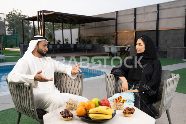 الجلوس في إحدى الشاليهات الاماراتية الراقية, رجل عربي خليجي اماراتي يرتدي الكندورة والغترة يقوم بتبادل الأحاديث مع زوجته في الهواء الطلق, قضاء أوقات عائلية ممتعة, التفاهم والترابط الفكري بين الزوجين، تنال الوجبات الخفيفة والتسالي