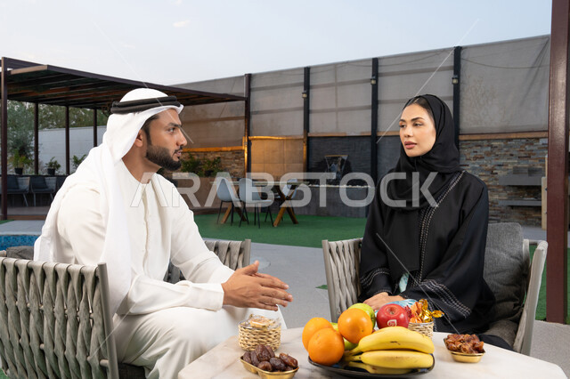 الجلوس في إحدى الشاليهات الاماراتية الراقية, رجل عربي خليجي اماراتي يرتدي الكندورة والغترة يقوم بتبادل الأحاديث مع زوجته في الهواء الطلق, قضاء أوقات عائلية ممتعة, التفاهم والترابط الفكري بين الزوجين، تنال الوجبات الخفيفة والتسالي