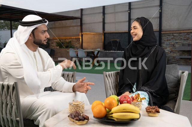 الجلوس في إحدى الشاليهات الاماراتية الراقية, رجل عربي خليجي اماراتي يرتدي الكندورة والغترة يقوم بتبادل الأحاديث مع زوجته في الهواء الطلق, قضاء أوقات عائلية ممتعة, التفاهم والترابط الفكري بين الزوجين، تنال الوجبات الخفيفة والتسالي