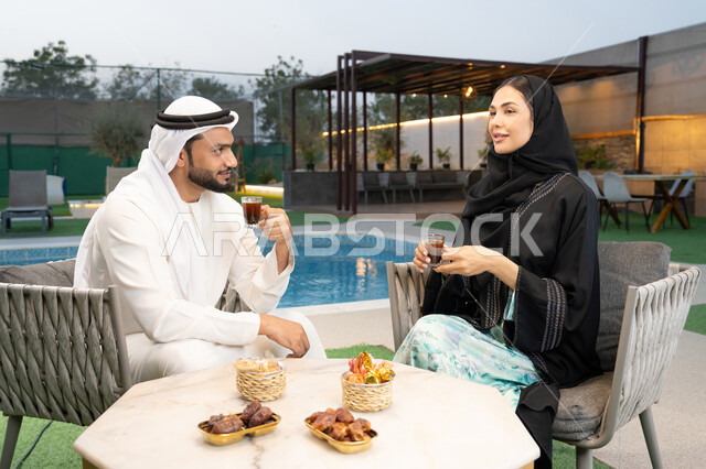 التفاهم والترابط الفكري بين الزوجين، تناول الوجبات الخفيفة والتسالي، الجلوس في إحدى الشاليهات الاماراتية الراقية، رجل عربي خليجي اماراتي يرتدي الكندورة والغترة يقوم بتبادل الأحاديث مع زوجته في الهواء الطلق، شرب القهوة العربية، قضاء أوقات عائلية ممتعة