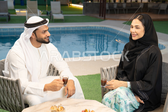 الجلوس في إحدى الشاليهات الاماراتية الراقية، رجل عربي خليجي اماراتي يرتدي الكندورة والغترة يقوم بتبادل الأحاديث مع زوجته في الهواء الطلق، شرب القهوة العربية، قضاء أوقات عائلية ممتعة، التفاهم والترابط الفكري بين الزوجين، تناول الوجبات الخفيفة والتسالي