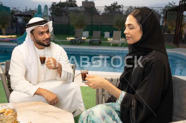التفاهم والترابط الفكري بين الزوجين، تناول الوجبات الخفيفة والتسالي، الجلوس في إحدى الشاليهات الاماراتية الراقية، رجل عربي خليجي اماراتي يرتدي الكندورة والغترة يقوم بتبادل الأحاديث مع زوجته في الهواء الطلق، شرب القهوة العربية، قضاء أوقات عائلية ممتعة