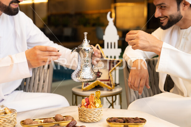 منتج وطني محلي اماراتي، زينة واضاءة رمضانية، عادات وتقاليد شرب القهوة التقليدية، الجلسة الليلة الخارجية في احدى شاليهات الامارات، حسن الاستقبال والكرم في شهر رمضان المبارك، صديقان عربيان خليجيان اماراتيان يرتديان الكندورة والغترة يجلسان في الهواء الطلق