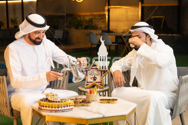 عادات وتقاليد شرب القهوة التقليدية، الجلسة الليلة الخارجية في احدى شاليهات الامارات، حسن الاستقبال والكرم في شهر رمضان المبارك، صديقان عربيان خليجيان اماراتيان يرتديان الكندورة والغترة يجلسان في الهواء الطلق، منتج وطني محلي اماراتي، زينة واضاءة رمضانية