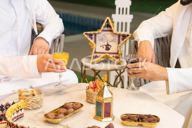 الجلسة الليلة الخارجية في احدى شاليهات الامارات، حسن الاستقبال والكرم، صورة مقربة لطاولة الضيافة في شهر رمضان المبارك، صديقان عربيان خليجيان اماراتيان يرتديان الكندورة والغترة يجلسان في الهواء الطلق، تبادل الاحاديث والاخبار بتعابير السرور، زينة واضاءة رمضانية