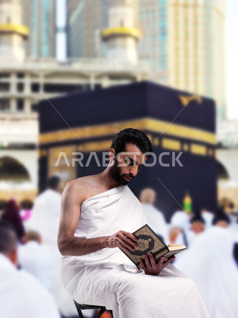 مفهوم العبادة والتقرب إلى الله تعالى، قراءة الأذكار والأدعية، أداء مناسك الحج و العمرة, أماكن و معالم دينة إسلامية مقدسة في المملكة العربية السعودية, رجل عربي خليجي سعودي يرتدي ملابس الاحرام يجلس امام الكعبه الشريفه يقرأ القران الكريم