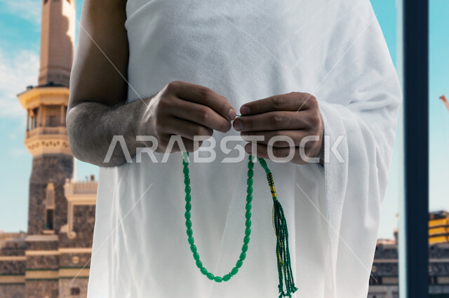 أداء مناسك الحج و العمرة, أماكن و معالم دينة إسلامية مقدسة في المملكة العربية السعودية, العبادة و التقرب إلى الله, صورة مقربة لرجل عربي خليجي سعودي يرتدي ملابس الاحرام يقف امام الكعبه المشرفه ممسكا بيده مسبحه ذات حبات خضراء