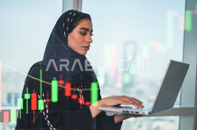 سيدة عربية خليجية سعودية تستخدم الحاسوب المحمول ، تراقب  صعود و نزول البورصة المالية ، الاستثمار المالي و الاقتصادي ، التطور الإقتصادي ، خلفية رسومات بيانية ثلاثية الأبعاد بتقنية الهولوجرام