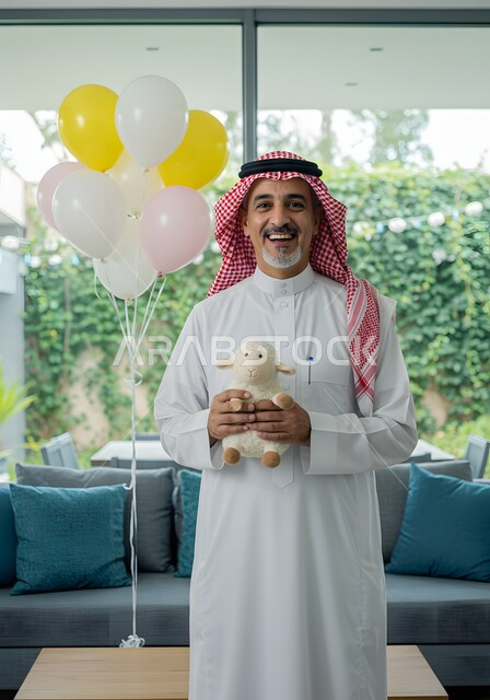 Gestures of joy, happiness and happiness, a smiling Saudi Arabian Gulf man wearing the traditional thobe and shemagh and holding a doll in the shape of a sheep for Eid al-Adha, Islamic holidays and occasions, celebrating the happy Eid at home