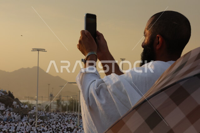 حاج يرتدي لباس الاحرام يقف على جبل عرفات، مفهوم العبادة والتقرب إلى الله، الحجاج والمعتمرين في مكة المكرمة، آدء مناسك الحج في يوم عرفة, مقصد المسلمين من أنحاء العالم, مكان ومعلم إسلامي ديني مقدس في المملكة العربية السعودية، موسم الحج 2025