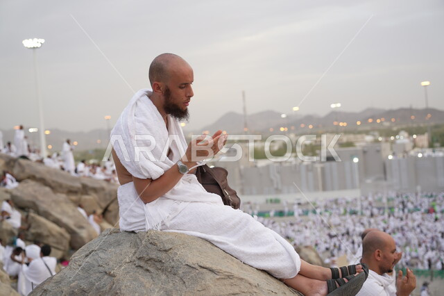 حاج يرتدي لباس الاحرام يقف على جبل عرفات، مفهوم العبادة والتقرب إلى الله، الحجاج والمعتمرين في مكة المكرمة، آدء مناسك الحج في يوم عرفة, مقصد المسلمين من أنحاء العالم, مكان ومعلم إسلامي ديني مقدس في المملكة العربية السعودية، موسم الحج 2025