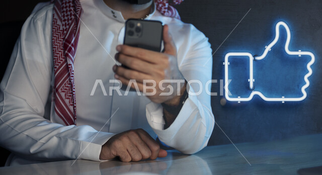 رجل عربي خليجي سعودي يحمل هاتف محمول بيده ، يتفاعل مع مواقع التواصل الإجتماعي السوشيال ميديا ، استخدام اللايك  ،  التفاعل مع العالم الافتراضي
