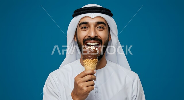  الحلويات الصيفية الباردة ، سكريات وأطعمة ذات سعرات حرارية عالية،  بوظة باردة في أجواء الصيف الحارة، بورتريه مقرب لرجل عربي خليجي اماراتي يرتدي الغترة والكندورة يمسك بيده بسكويت الأيس كريم بنكهة الفواكه، خلفية زرقاء