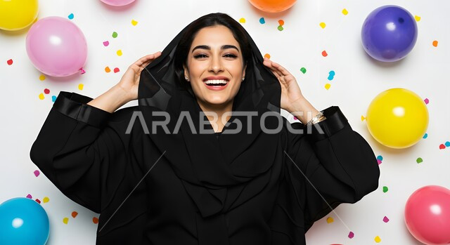زينة وبلالين ومفرقعات ورقية ملونة، صورة مقربة لإمرأة عربية خليجية سعودية ترتدي العباءة والحجاب تقف بتعابير وايماءات السرور والبهجة، الاحتفال بالمناسبات وأعياد الميلاد