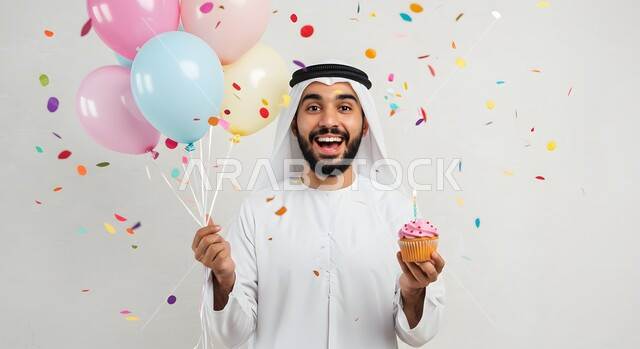  الاحتفال بالمناسبات وأعياد الميلاد، زينة وبلالين ومفرقعات ورقية ملونة، صورة مقربة لرجل عربي خليجي اماراتي يرتدي الكندورة والغترة يمسك بيده قطعة الكاب كيك الشهية المزينة بالكريمة المخفوقة، أطعمة وحلويات لذيذة، معجنات طازجة مخبوزة في الفرن
