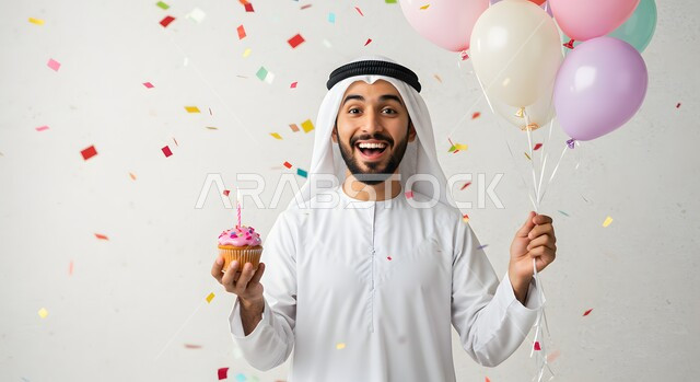  الاحتفال بالمناسبات وأعياد الميلاد، زينة وبلالين ومفرقعات ورقية ملونة، صورة مقربة لرجل عربي خليجي اماراتي يرتدي الكندورة والغترة يمسك بيده قطعة الكاب كيك الشهية المزينة بالكريمة المخفوقة، أطعمة وحلويات لذيذة، معجنات طازجة مخبوزة في الفرن