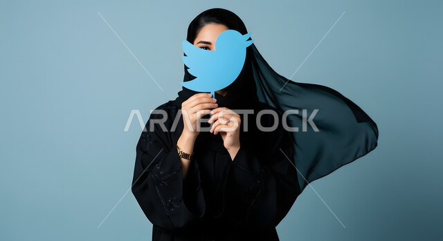 تطبيقات الهاتف المحمول، تصفح وسائل التواصل الاجتماعي، بورتريه مقرب لإمرأة عربية خليجية سعودية ترتدي الحجاب والعباءة تمسك بيدها شعار تطبيق تويتر، ايقونة برنامج السوشل ميديا، خلفية زرقاء