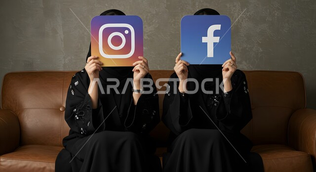 تطبيقات الهاتف المحمول، تصفح وسائل التواصل الاجتماعي، بورتريه لإمرأتين عربيتين خليجيتين سعوديتين ترتديان العباءة تجلسان على الكنبة تمسكان بيدهما شعار تطبيق فيسبوك وانستاغرام، ايقونة برنامج السوشل ميديا، خلفية رمادية