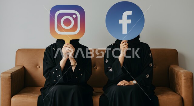 Mobile apps, social media browsing, portrait of two Saudi Arabian Gulf women wearing abaya sitting on a sofa holding Facebook and Instagram logo, social media icon, gray background