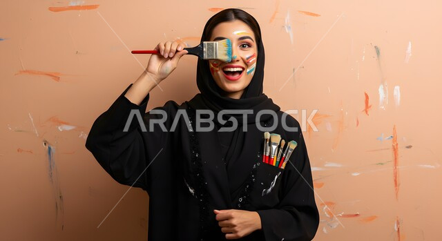 Learning, creativity and skill development, having fun, the concept of femininity and softness, a close-up of a Saudi Arabian Gulf woman wearing a hijab holding a watercolor brush in her hand standing in an art workshop, learning and the passion of love for drawing