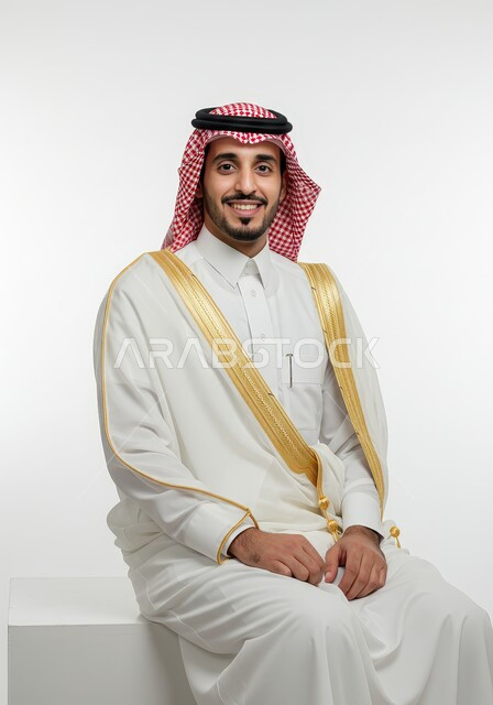 الشعور بالثقة في النفس، الاهتمام بالأناقة والمظهر الخارجي، بورتريه لرجل عربي خليجي سعودي مبتسم يرتدي الشماغ والثوب التقليدي والبشت الابيض ينظر إلى الكاميرا بإيماءات وتعابير السرور والسعادة، خلفية بيضاء