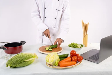 احترافية تقطيع الخضار، شغف التدرب على مهارة الطهي وإعداد الطعام، بورتريه مقرب لرجل عربي خليجي اماراتي يرتدي زي العمل يحضر طبق صحي مفيد، شيف سعودي يقوم بتحضير سلطة الخضراوات الطازجة، استخدام المكونات والمقادير المناسبة للوجبة، خلفية بيضاء