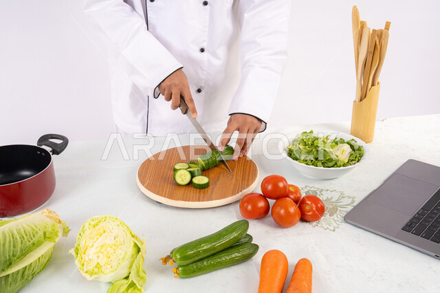 حب التدرب على مهارة الطهي وإعداد الطعام، احترافية تقطيع الخضار، بورتريه مقرب لرجل عربي خليجي اماراتي يرتدي زي العمل يحضر طبق صحي مفيد، شيف سعودي يقوم بتحضير سلطة الخضراوات الطازجة، استخدام المكونات والمقادير المناسبة للوجبة، خلفية بيضاء